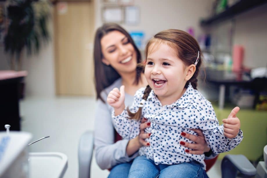 child laughing on parent's lap in dental office